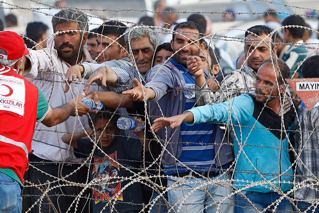 A member of the Turkish Red Crescent distributes water to Syrian Kurds as they wait behind the border fences to cross into TurkeyReuters