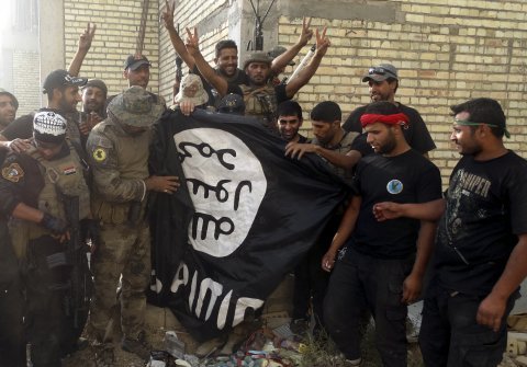 Iraqi security forces stand with an Islamist State flag which they pulled down at the University of Anbar, in Anbar province July 26, 2015.Reuters